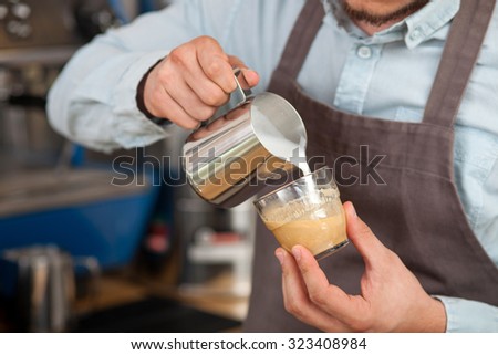 Close up of hands of cafeteria worker making late. The man is holding a cup and pouring milk into it carefully