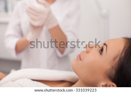 Close up of arms of cosmetologist clapping her hands with joy. The result of done procedure is great. Her female customer with perfect skin is sitting and relaxing
