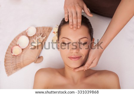 Close up of arms of masseuse massaging female forehead and chin. The young beautiful woman is getting head massage with pleasure. She is lying and smiling