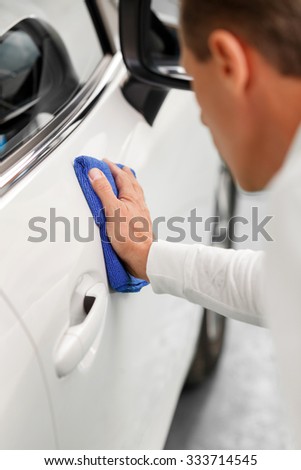 Close up of experienced mid aged mechanic washing the car with a cloth. He is kneeling and looking a transport with concentration