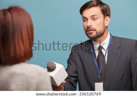 Cheerful male tv reporter is asking the woman to give his the interview. He is holding a microphone and stretching in forward. The man is standing and listening attentively. Isolated
