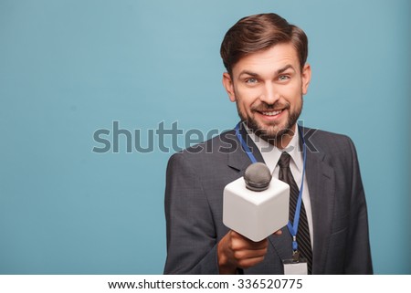 Attractive young tv journalist is interviewing someone with joy. He is standing and stretching a microphone forward. The man is looking at camera and smiling. Isolated and copy space in left side