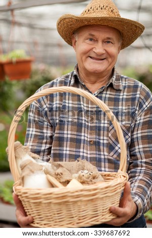 Professional old farmer is presenting a basket of milk and eggs. The man is standing in his garden and smiling. He is looking at camera happily