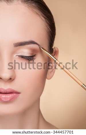 Close up of half of the female face. The beautiful woman is getting make up by artist. The beautician is touching a brush to her eyebrow. The girl closed eyes with calmness