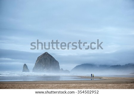 Young couple is walking with dog along Cannon Beach near Haystack Rock in Pacific Ocean