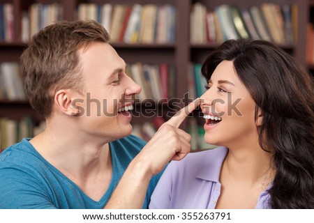 I like spending time with you. Beautiful young loving couple is dating and embracing in the library. They are laughing. The man is touching female nose with joy