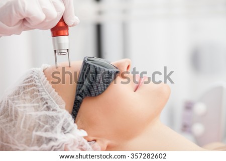 Close up of hands of professional beautician making skin treatment for woman. The lady is smiling with relaxation. She is lying and wearing goggles