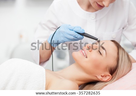 Cheerful young girl is getting facial treatment by beautician. She is smiling. The lady is lying with relaxation