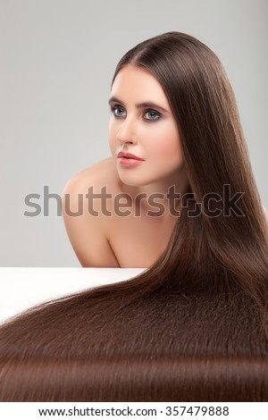Cute girl is caring of her hair. She is putting it on the surface to show it is long and straight. The lady is looking forward with confidence. Isolated