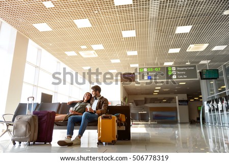 Happy young loving couple is sitting and drinking coffee at airport lounge. They are embracing and smiling