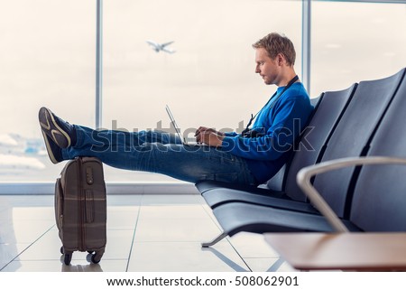 Sending quick text before take-off. Handsome young man sitting at airport and enjoying his laptop while waiting landing