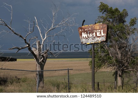 Rusty old motel sign with bullet holes next to an old tree, with a storm in the background, in eastern Colorado.