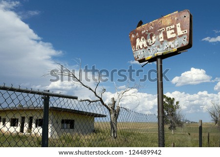 Old, rust motel sign with bullet holes, with a creepy tree, gutted building, and storm clouds in the background in a forgotten town in eastern Colorado.