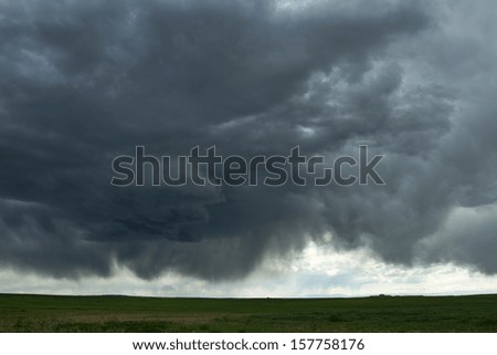 Cumulus clouds and virga of a massive thunderstorm, over a green meadow in Colorado.