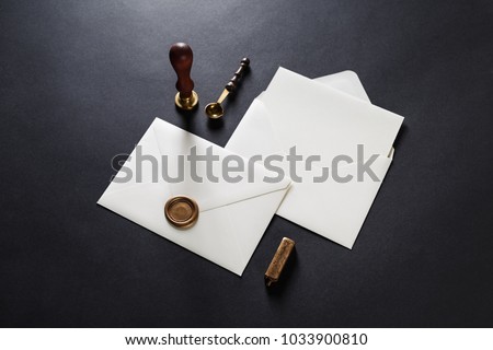 Blank paper envelopes with golden wax seal, stamp, spoon and postcard on black paper background. Mockup for your design.