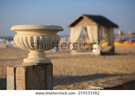 Old plaster vase in antique style on a background of a sandy beach and a canopy. Shallow depth of field.