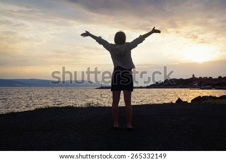 Silhouette of a girl with raised hands on the background of sunrise over the sea. Focus on model. Shallow depth of field. Toned image.