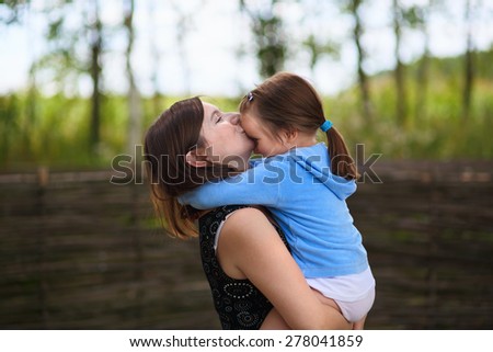 A mother\'s love. Mom keeps little daughter in her arms and kisses her on the forehead. Selective on the faces of the models.