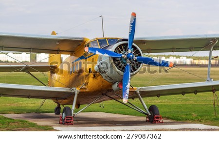 Old yellow vintage single-engined biplane with blue propeller. The plane on a background of green grass. Selective focus.