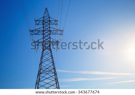 Electricity pylon silhouetted against blue sky background. High voltage tower.