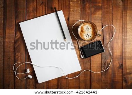 Blank paperwork template for designers. Responsive design mockup on vintage wooden background. Paper, letterhead, coffee cup, smartphone, pencil and headphones on wooden table background. Top view.