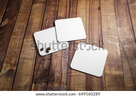 Blank square beer coasters and coffee beans on vintage wood table background. Responsive design mockup.