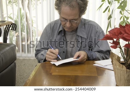 Older man writing checks/Senior Paying Bills/Senior working in the early afternoon on his finances
