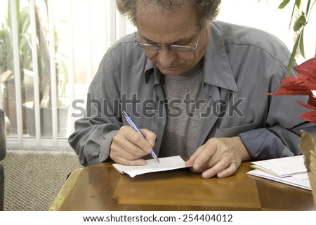 Older man writing checks/Senior Paying Bills/Senior working in the early afternoon on his finances