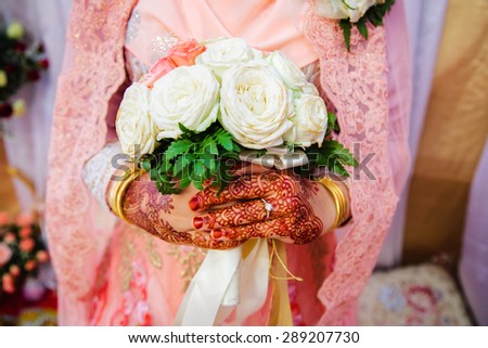 close up of  bride\'s hand with henna painted wearing wedding ring holding a rose bouquet in traditional Islamic wedding