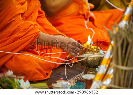 close up of buddhist monk\'s hand pouring melt candle tears to the water for making blessing water