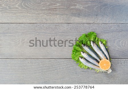 Five fresh sardines in heart form laying on green lettuce with slice of lemon, wooden table