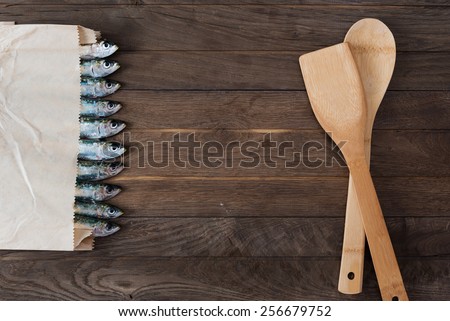 Paper bag with sardines in line on one side and kitchen utensils on other side of wooden table