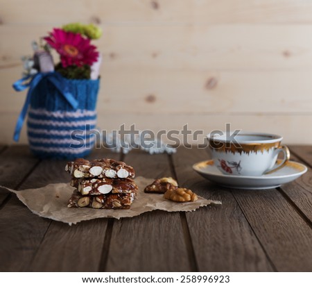 Nut bar with nuts, coffee cup and small bouquet in knitted vase on old wooden table