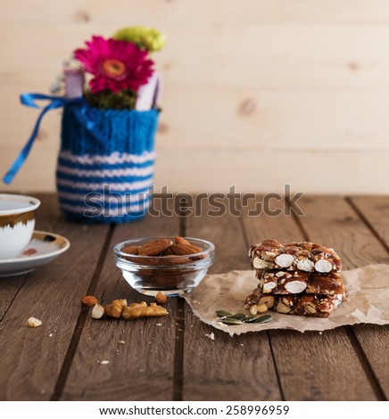 Nut bar with nuts, coffee cup and small bouquet in knitted vase on old wooden table