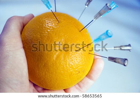 Hand holding an orange with multiple syringe needles - pin cushion.