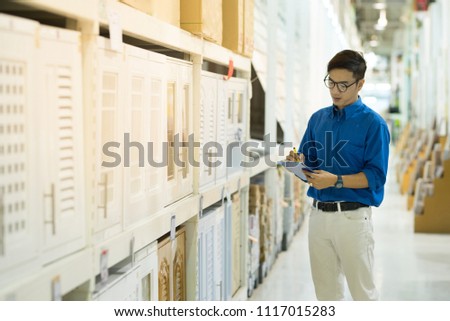 Young Asian man standing checking the shopping list and looking for product in warehouse wholesale, shopping warehousing concept