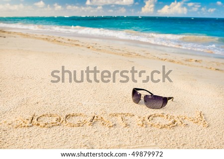 Black sun glasses on white sand beach and word vocation near blue sea