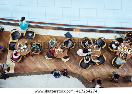 Top view of many people sitting in food court cafe eating lunch near artificial ice rink. City cafe. People having lunch at city cafe. People eating business lunch during work day. Aerial cafe lunch.