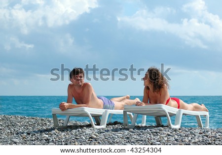 Young man and woman lies in chaise lounge on beach