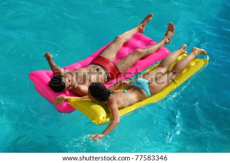 Happy young woman and the man floating on a mattress in water pool