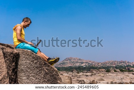 Young man sitting on the mountain with beautiful view and working on the laptop.