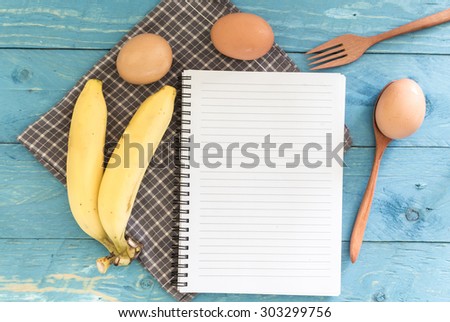 Recipe book with banana and egg on wooden background