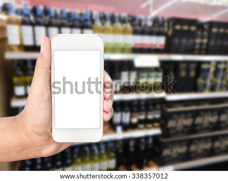 Hand holding mobile smart phone on wine Liquor bottle on shelf, Blurred background