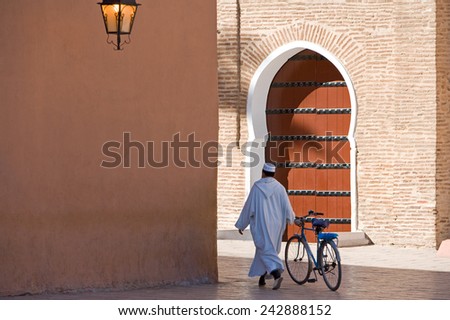 Marrakesh, Morocco - March 2006: A local man with bicycle walking in front of the side door of the great Koutoubia mosque