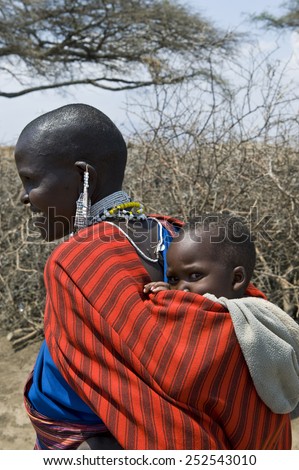 Ngorongoro, Tanzania - September 1 2008: A smiling mother with traditional jewels carries on her shoulders a child in a Masai village