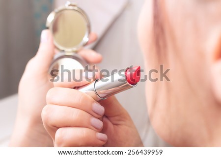Female hands holding lipstick and small silver mirror
