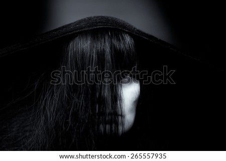 Low key black and white portrait of a mysterious woman representing a witch. Focus on a hair, face is mostly hidden.