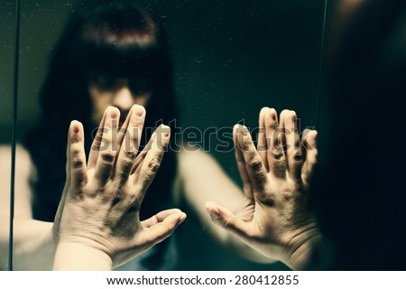 Dark haired, mysterious woman looking her reflection in a mirror.