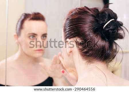 Young brunette watching her reflection in mirror, touching mirror with hand
