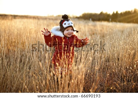 Cute toddler in a field at sunset having fun in her red winter coat and penguin hat.